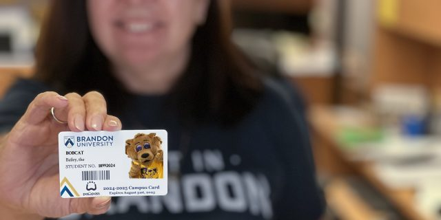 A woman holds a student ID card. The card features the university mascot, a cartoon bobcat named Bailey.