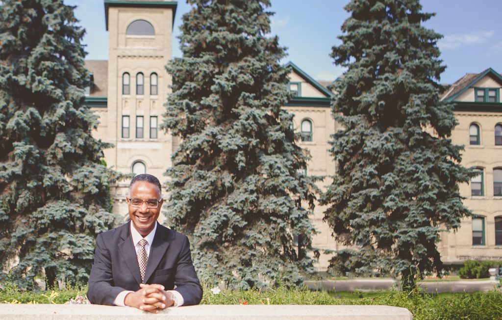 President Dr. Gervan Fearon poses in front of historic Clark Hall at Brandon University.
