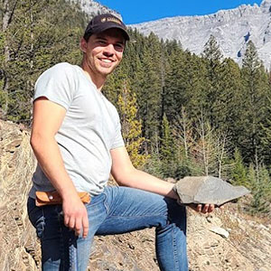 Zach Toews standing on a rock pile holding a rock sample 