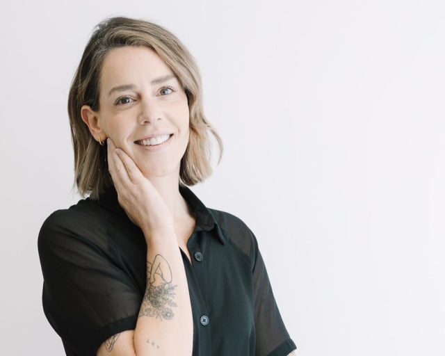 A woman poses with a smile in front of a white background